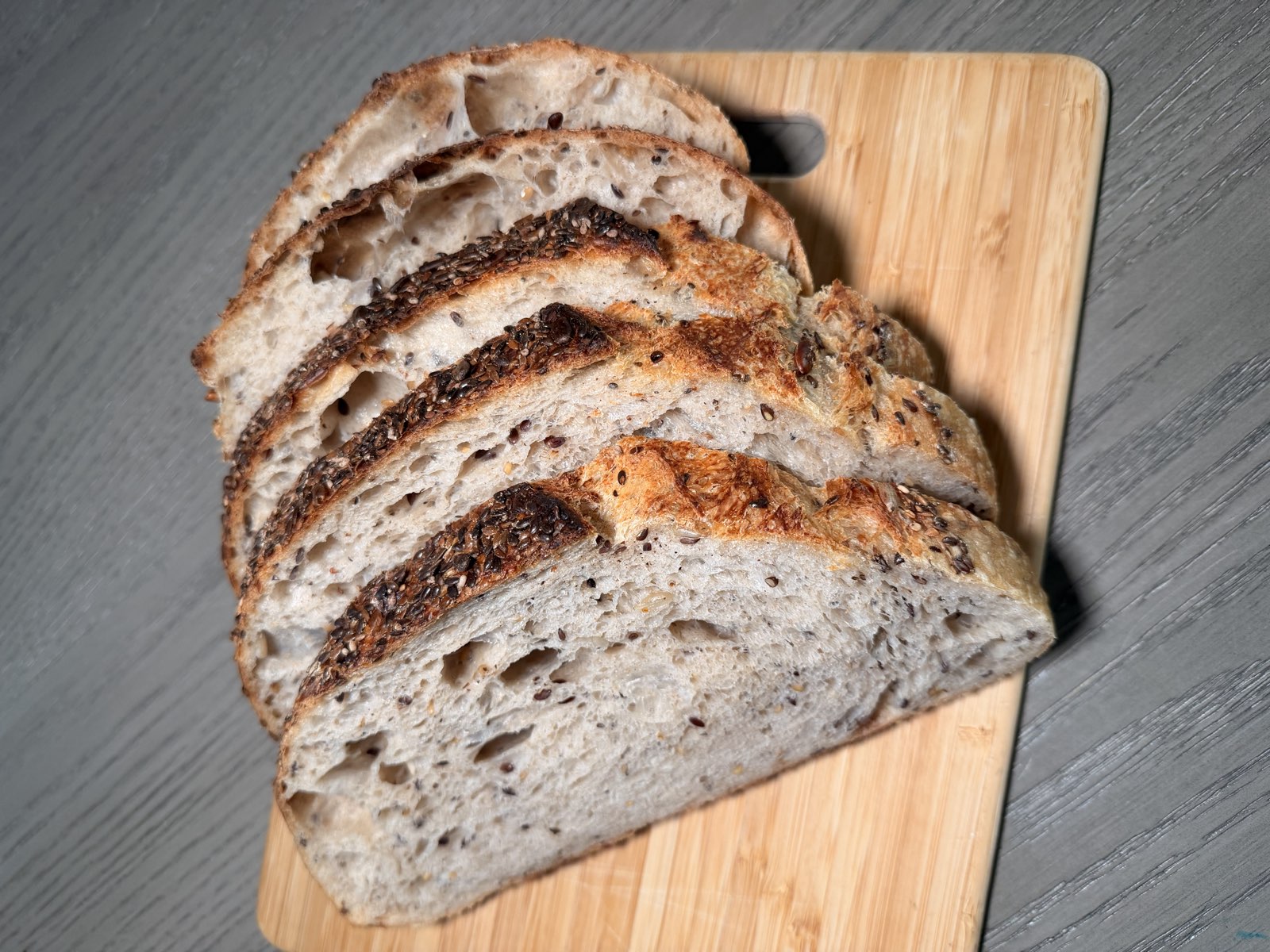 Sliced artisan sourdough loaf with a seeded crust, fanned on a wooden board